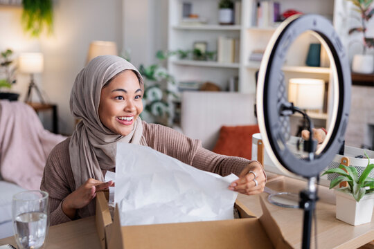 Woman in hijab unboxing package for online video.