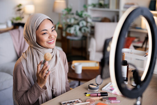 Woman in hijab applies makeup in front of ring light.
