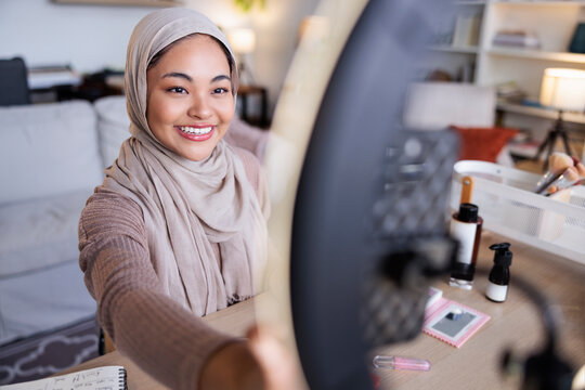 Smiling woman in hijab films beauty tutorial.