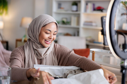 Woman in hijab smiles while unboxing a package.