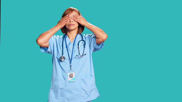 Healthcare expert covering eyes, ears and mouth with hands, imitating the three wise monkeys. Licensed nurse showing don t see, don t hear and don t speak concept, isolated over studio background