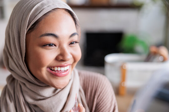 Smiling woman in hijab holds lip gloss applicator.