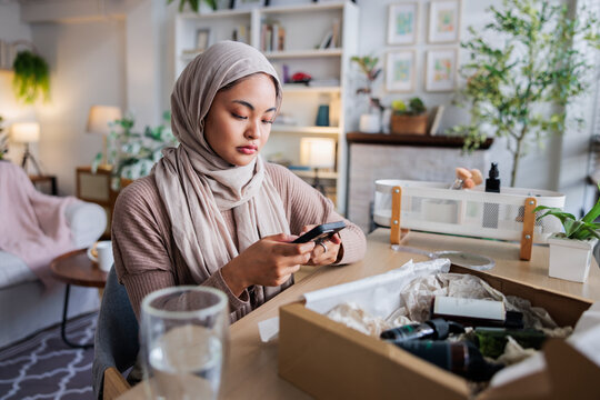 Woman in hijab uses phone near beauty product box.
