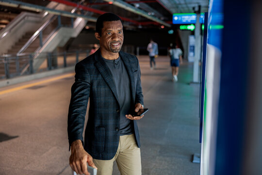 Man with phone and luggage at train station.