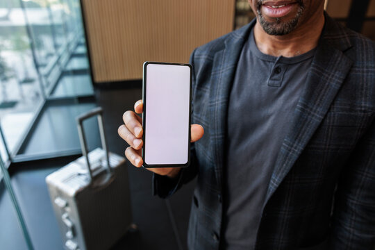 Man with suitcase shows blank smartphone screen.