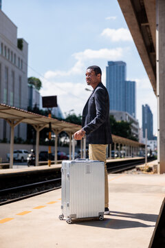 Man with suitcase waits at train station platform.