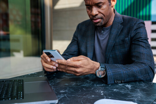 Man in suit uses phone at table with laptop.