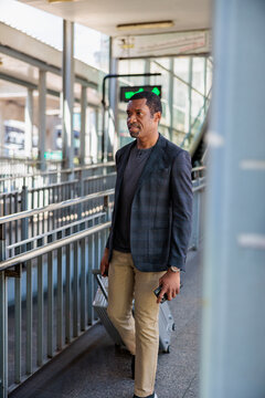 Man with suitcase and phone at train station.
