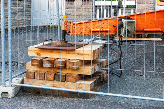 Stacked wooden cribbing supporting crane outrigger behind safety fence. Heavy equipment support and stability setup.

