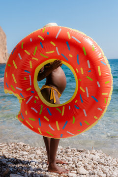 Black woman standing near sea with donut floater 