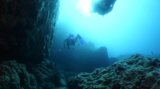  scuba divers exploring   reefs walls and caverns  underwater deep blue water big rocks and bubbles ocean scenery 