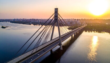 Obraz premium Aerial view captures a suspension bridge at sunrise. The sun casts a warm glow over the cityscape and water