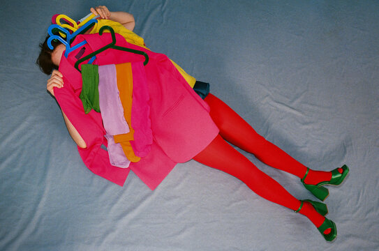 Person Lying on Blue Fabric Covered with Bright Clothes on Hangers