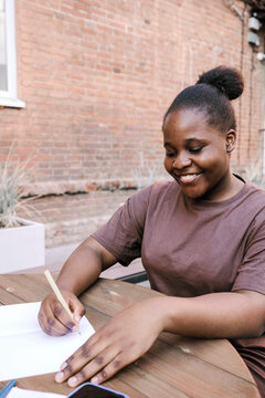 A girl writes on paper outside during the day.