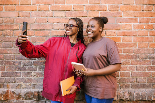 Two friends take a photo near a brick wall.