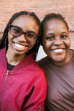 Two friends are smiling near a brick wall.