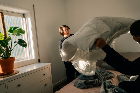 Two People Making a Bed in a Brightly Lit Room With Plants