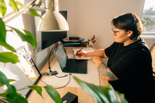 Person Working at Desk With Laptop and Plant Nearby in Home Office