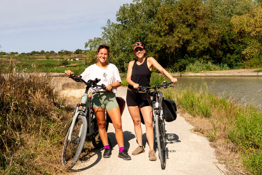 Two sisters happy cyclists posing with bikes on sunny canal path