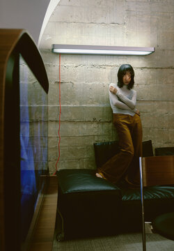 Asian woman in fashionable attire is standing on a sofa