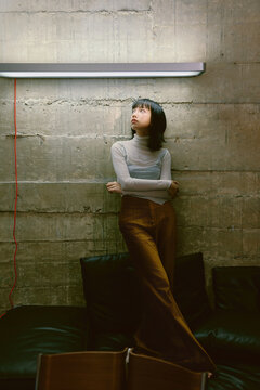 Asian woman in fashionable attire is standing on a sofa