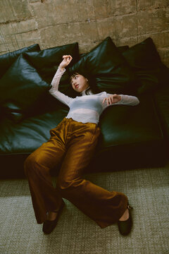 An Asian woman, dressed in fashionable attire, lying on the sofa