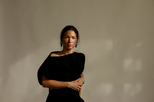 A Woman Sits in a Wooden Chair, Her Arms Crossed