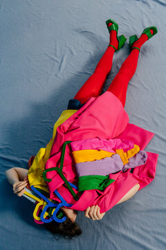 Person Lying on Blue Fabric Covered with Bright Clothes on Hangers