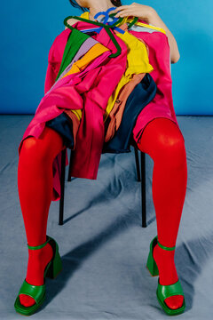 Seated Figure Holding Bright Clothes on Hangers in Studio Setting