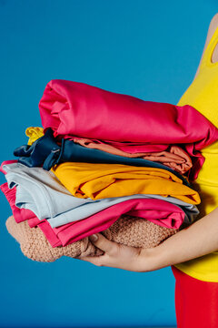 Stack of Bright Folded Clothes in Hands on Blue Background