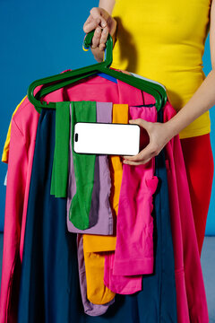 Person Holding Colorful Clothes on Hangers and Phone With Blank Screen