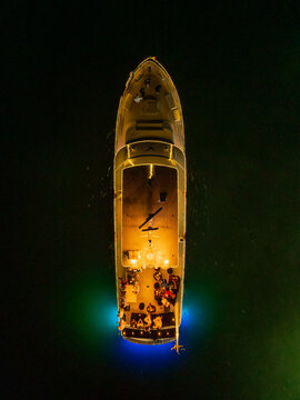 Aerial view of a luxury yacht at night off the Peninsula de Yucatan with glowing deck lights, people on deck, and vibrant blue underwater illumination Yucatan, Mexico.