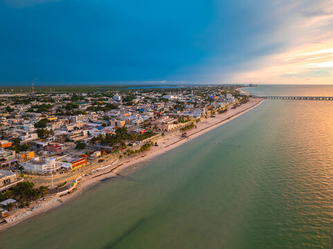 Aerial view of the coastal town and long pier along the sandy beach and turquoise water under a dramatic sunset sky Yucatan, Mexico.