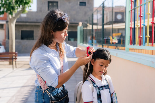 Mother Fixes Daughter's Hair Before School in the Playground