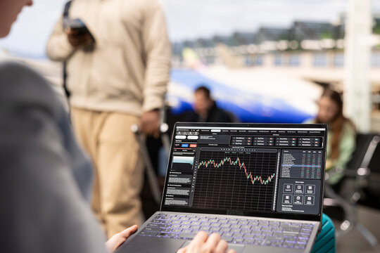 Digital nomad woman analyzing financial trends and stock market data on laptop in airport terminal lounge, waiting for flight boarding. Reviewing candlestick charts and forex exchange rates.