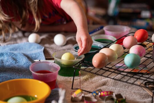 Child dipping Easter egg into dye with decorated eggs drying on rack