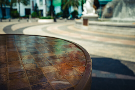 Close-up of a tiled outdoor cafe table with a blurred fountain background.