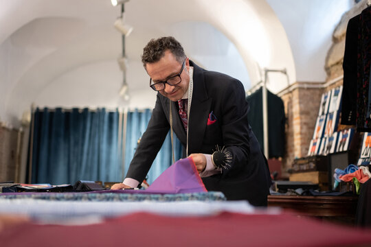 Mature male tailor inspecting cloth in studio