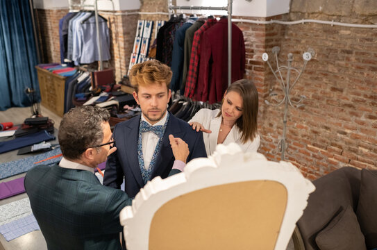 Tailor and assistant fitting suit on client