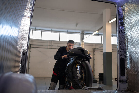 Middle aged male motorcyclist unloading motorbike from truck