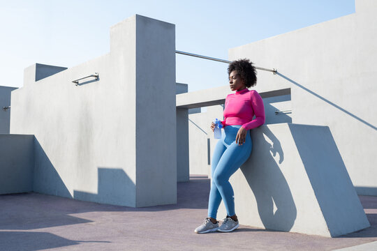 Black sportswoman with water leaning on wall