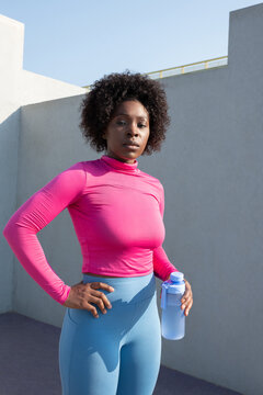 Black sportswoman with water against wall