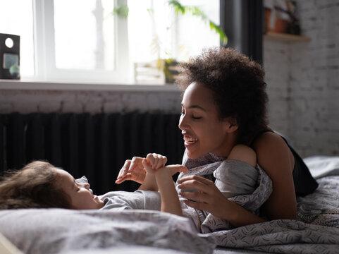 Ethnic mother playing with daughter after awakening