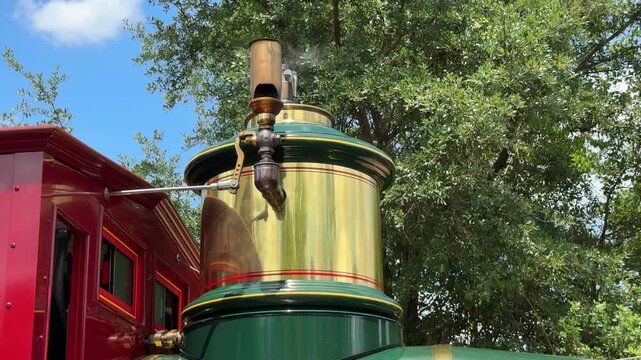A vintage steam train boiler and chimney are shown in close view against green trees. The image represents historic railway transportation and classic engineering.