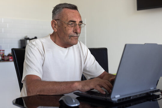 elderly senior man uses internet on laptop computer, wears glasses