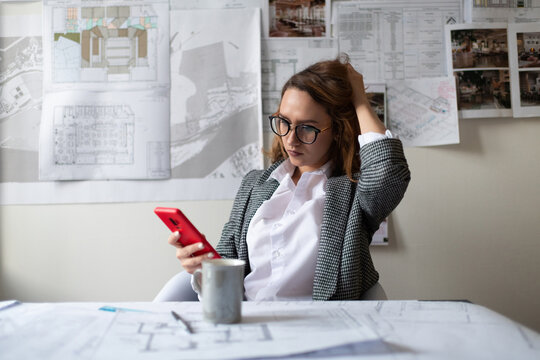 Thoughtful female architect browsing smartphone in office