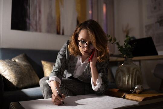 Tired architect making notes of blueprint during call to client