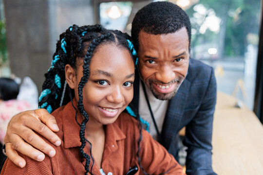 Smiling father and daughter pose together indoors.