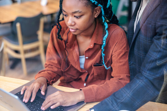 Woman with blue braids works on laptop with mentor.