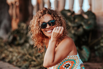 Smiling woman with curly hair wearing sunglasses and a colorful crochet top outdoors